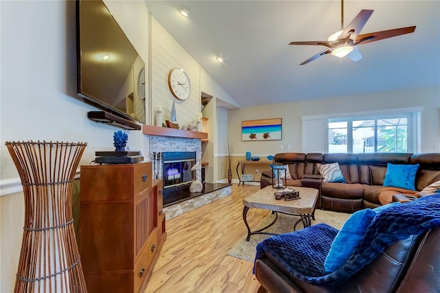 living area with baseboards, light wood-style flooring, ceiling fan, a stone fireplace, and vaulted ceiling