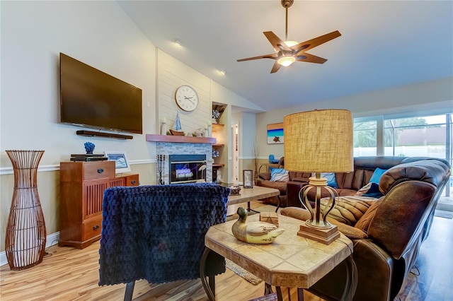 living room with high vaulted ceiling, ceiling fan, light hardwood / wood-style floors, and a stone fireplace