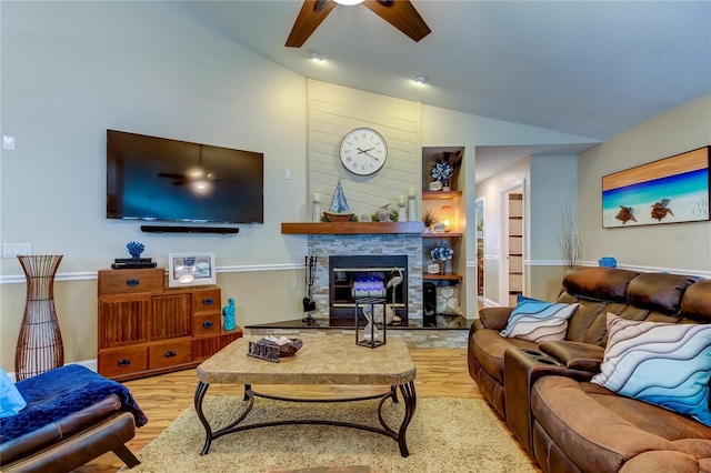 living room with light wood-type flooring, a stone fireplace, ceiling fan, and vaulted ceiling