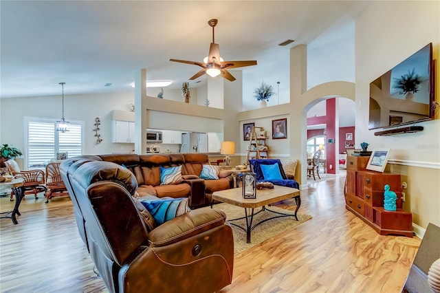 living area featuring arched walkways, ceiling fan with notable chandelier, light wood finished floors, and a healthy amount of sunlight