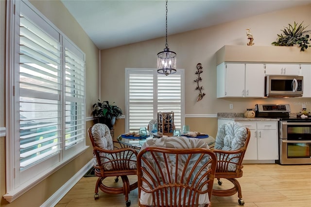 dining space featuring light wood-type flooring, an inviting chandelier, and vaulted ceiling