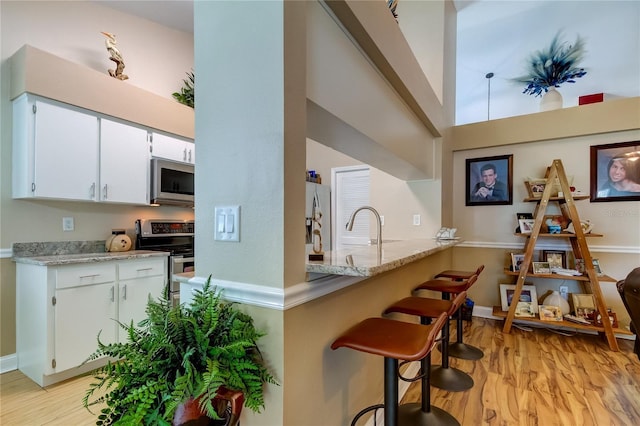 kitchen featuring light stone countertops, a breakfast bar, appliances with stainless steel finishes, light wood-style floors, and white cabinetry