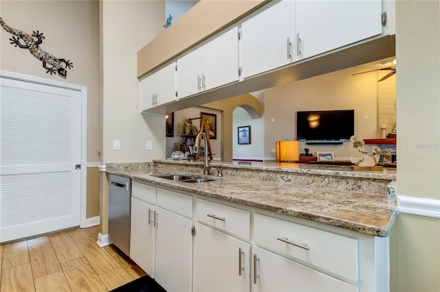 kitchen featuring light wood-style flooring, arched walkways, a sink, white cabinets, and dishwasher