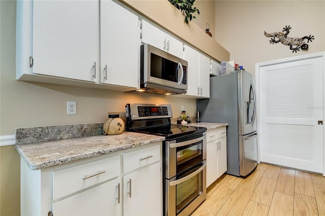 kitchen with light stone countertops, stainless steel appliances, white cabinets, and light hardwood / wood-style floors