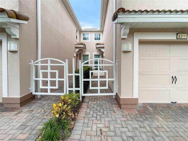 view of exterior entry with stucco siding, a tile roof, and a gate