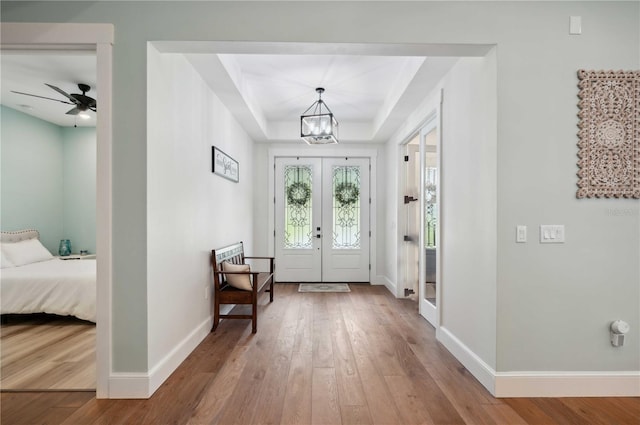 foyer entrance with a raised ceiling, french doors, ceiling fan with notable chandelier, and hardwood / wood-style flooring