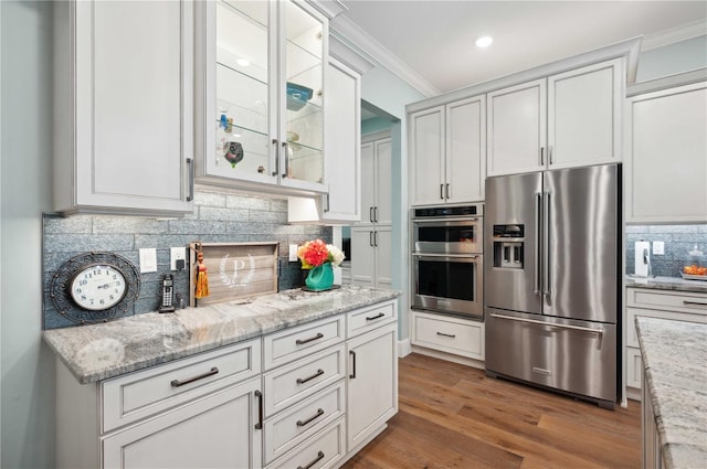 kitchen with light stone countertops, appliances with stainless steel finishes, crown molding, hardwood / wood-style floors, and white cabinetry