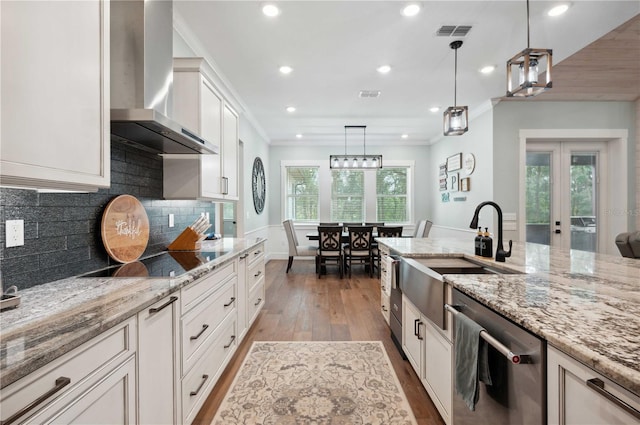 kitchen featuring french doors, wall chimney exhaust hood, hardwood / wood-style flooring, dishwasher, and hanging light fixtures