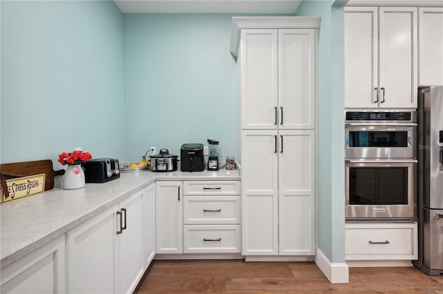 kitchen featuring white cabinets, hardwood / wood-style floors, stainless steel appliances, and light stone counters