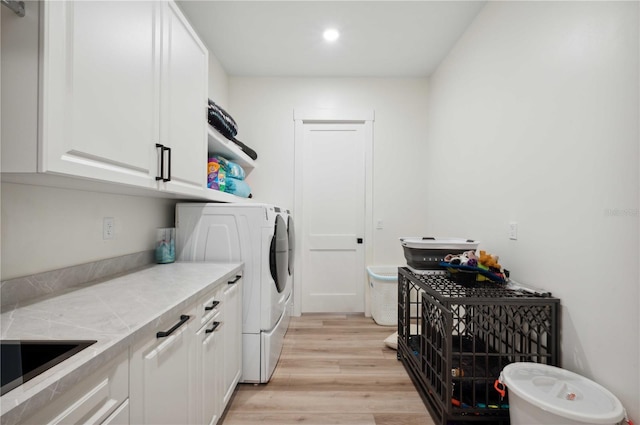 washroom featuring washer and dryer, cabinets, sink, and light hardwood / wood-style flooring