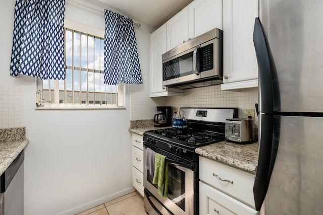 kitchen with appliances with stainless steel finishes, light tile patterned flooring, light stone countertops, and white cabinets