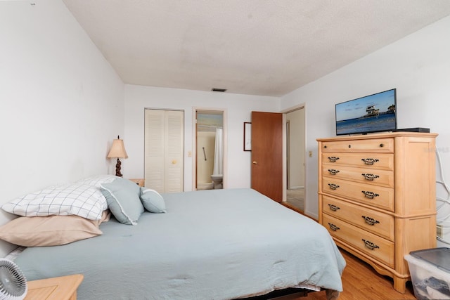 bedroom with ensuite bath, a textured ceiling, light hardwood / wood-style flooring, and a closet