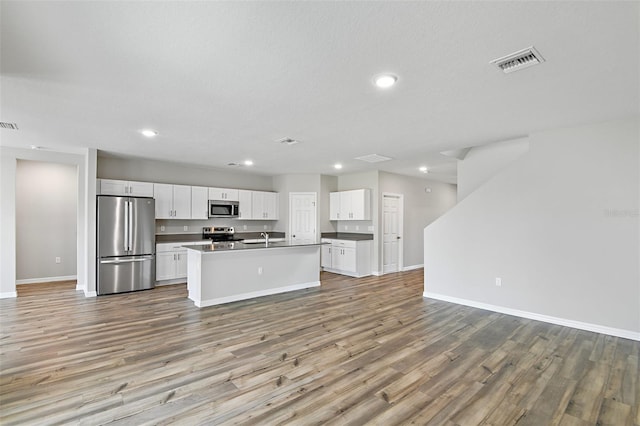 kitchen with an island with sink, light hardwood / wood-style flooring, appliances with stainless steel finishes, and white cabinetry