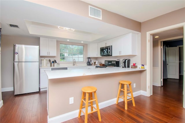 kitchen with white cabinets, appliances with stainless steel finishes, a kitchen bar, and a raised ceiling