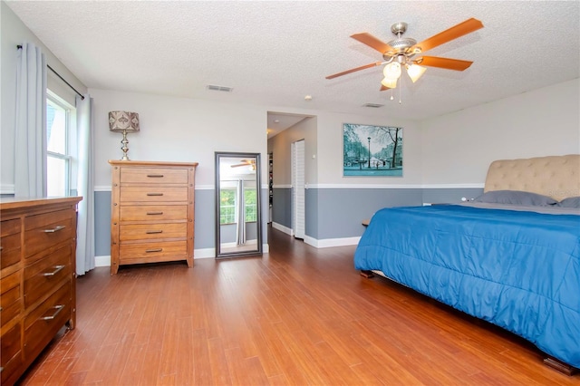 bedroom with a textured ceiling, ceiling fan, multiple windows, and hardwood / wood-style flooring