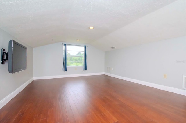 additional living space with hardwood / wood-style flooring, a textured ceiling, and vaulted ceiling