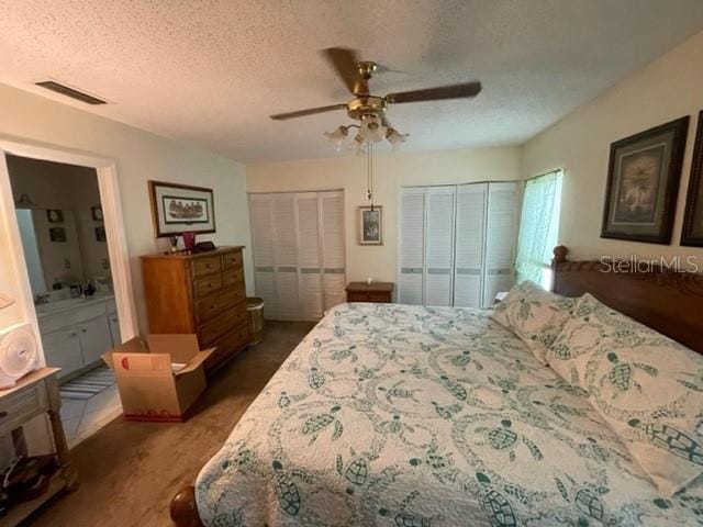 carpeted bedroom featuring a textured ceiling, multiple closets, ensuite bath, and ceiling fan