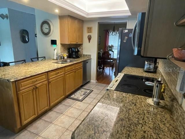 kitchen with stainless steel appliances, decorative backsplash, a chandelier, a raised ceiling, and crown molding