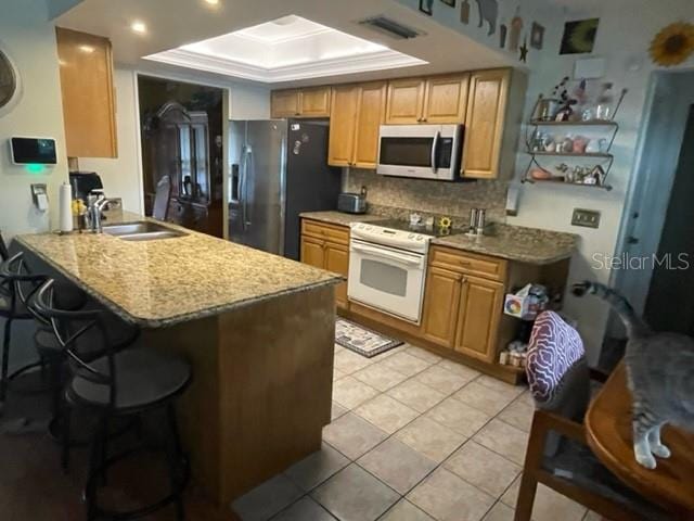 kitchen with stainless steel appliances, a breakfast bar, light stone counters, kitchen peninsula, and a raised ceiling