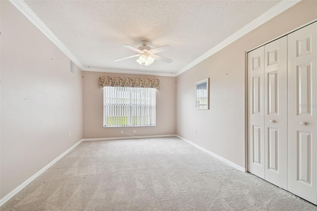 spare room with a textured ceiling, light colored carpet, ceiling fan, and ornamental molding