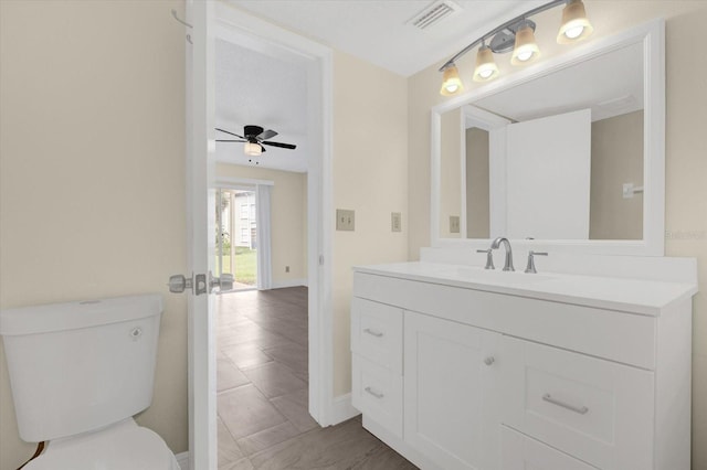 half bath featuring visible vents, toilet, vanity, and a ceiling fan