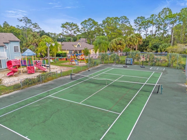 view of tennis court featuring playground community and fence