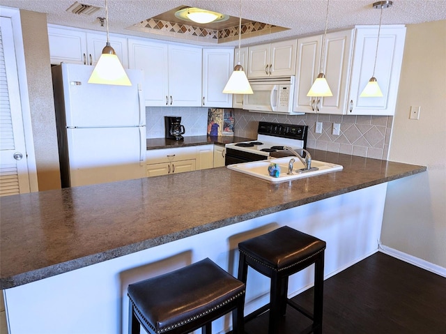 kitchen featuring kitchen peninsula, white cabinetry, a kitchen bar, pendant lighting, and white appliances