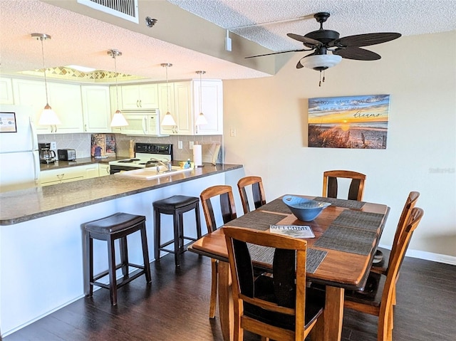 dining space featuring dark wood-type flooring, ceiling fan, and a textured ceiling