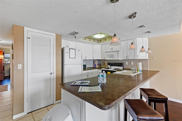 kitchen featuring kitchen peninsula, a breakfast bar, sink, decorative light fixtures, and white appliances