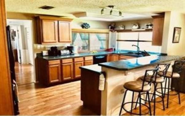 kitchen featuring light hardwood / wood-style floors, sink, a textured ceiling, black dishwasher, and a kitchen bar