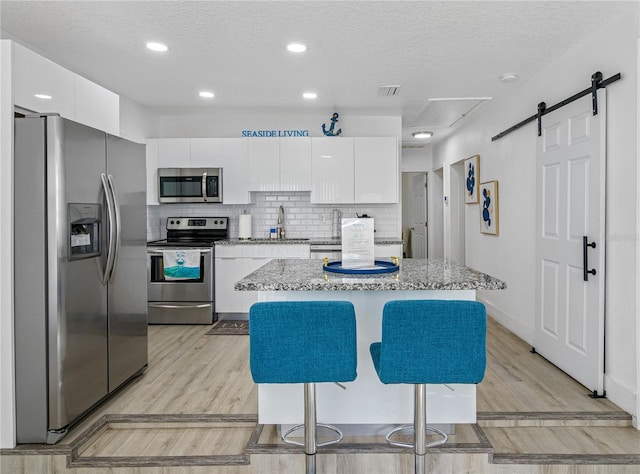 kitchen featuring white cabinetry, stainless steel appliances, a barn door, a breakfast bar area, and a kitchen island