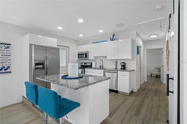 kitchen featuring a kitchen bar, appliances with stainless steel finishes, a textured ceiling, white cabinets, and a kitchen island