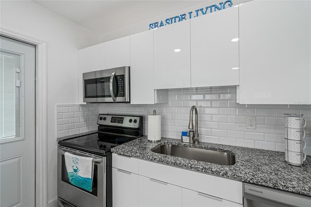 kitchen with backsplash, dark stone counters, stainless steel appliances, sink, and white cabinets