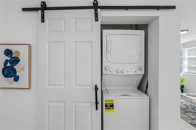 clothes washing area with a textured ceiling, stacked washer / dryer, and a barn door