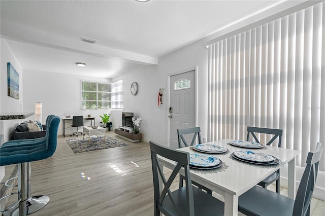 dining space with beam ceiling, light hardwood / wood-style floors, and a textured ceiling