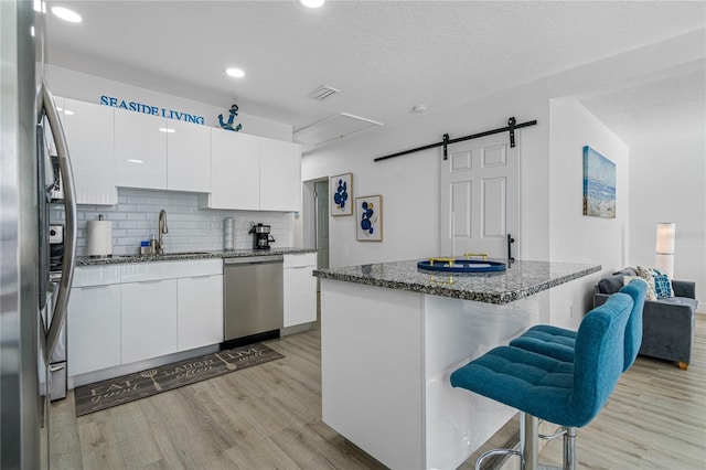 kitchen featuring white cabinetry, sink, a barn door, a breakfast bar, and appliances with stainless steel finishes