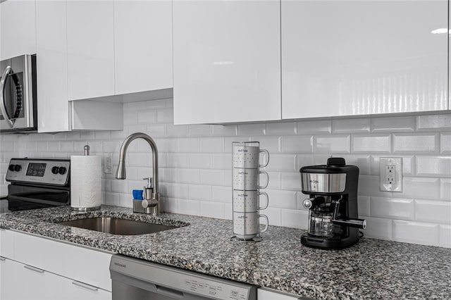 kitchen featuring tasteful backsplash, dark stone counters, stainless steel appliances, sink, and white cabinetry