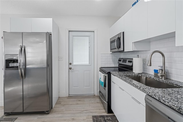 kitchen with stainless steel appliances, white cabinetry, dark stone counters, and sink