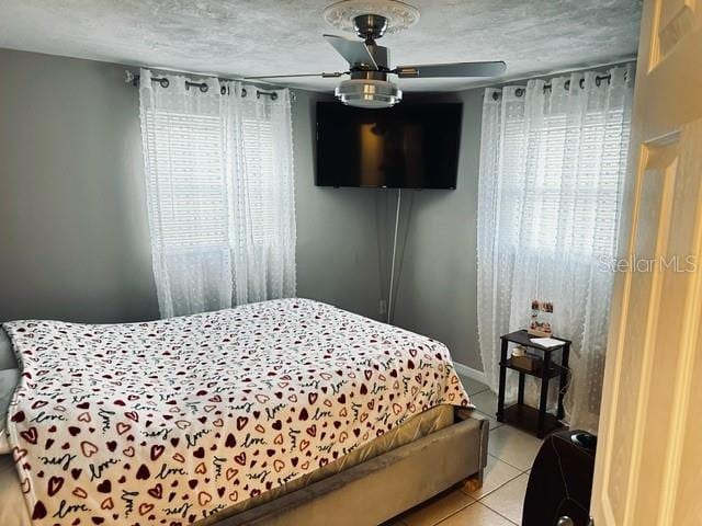 tiled bedroom featuring multiple windows, ceiling fan, and a textured ceiling