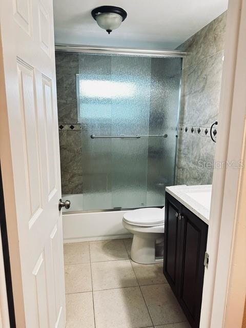 full bathroom featuring enclosed tub / shower combo, vanity, toilet, and tile patterned floors