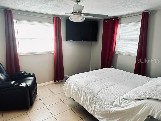 bedroom with a textured ceiling, light tile patterned floors, and ceiling fan