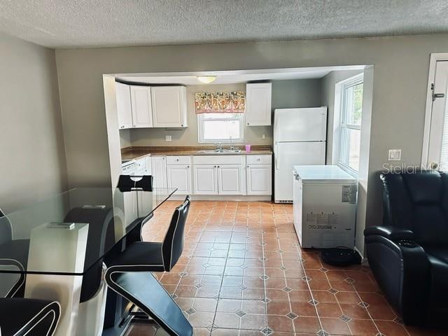 kitchen featuring white refrigerator, sink, a textured ceiling, and white cabinetry