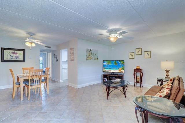 living room with visible vents, a textured ceiling, light tile patterned floors, baseboards, and ceiling fan