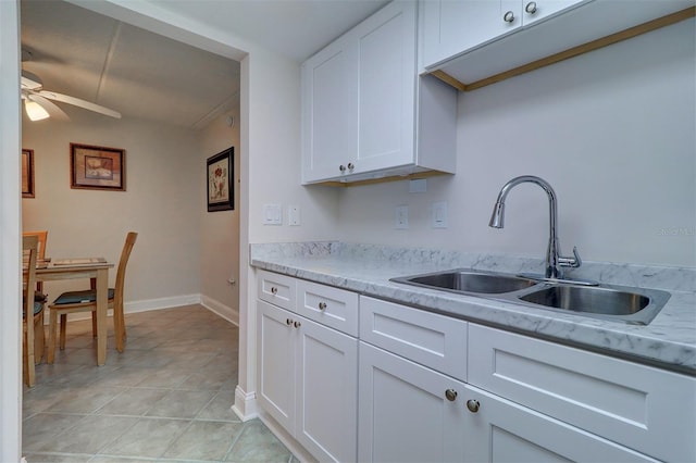 kitchen with baseboards, light tile patterned floors, white cabinets, a ceiling fan, and a sink