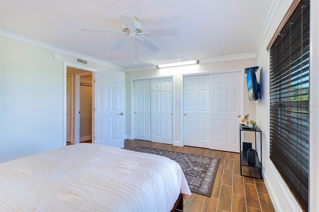 bedroom with ornamental molding, wood-type flooring, two closets, and ceiling fan