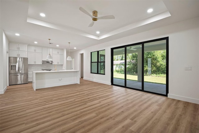 unfurnished living room featuring a raised ceiling, light hardwood / wood-style flooring, and ceiling fan