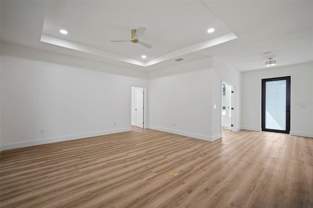 empty room featuring light wood-type flooring, ceiling fan, and a raised ceiling