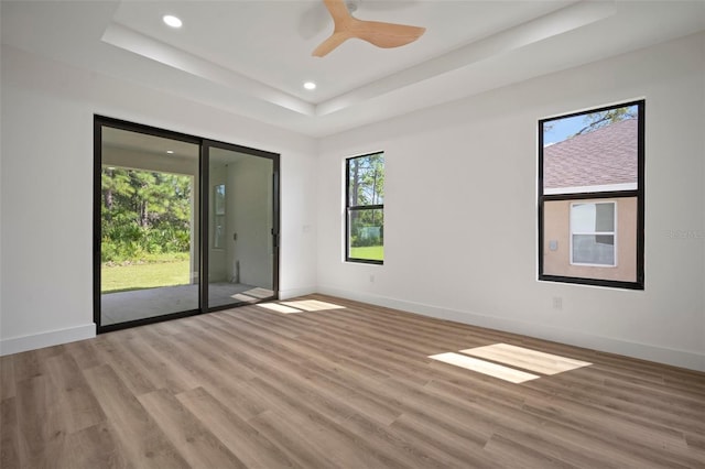 unfurnished room with a raised ceiling, hardwood / wood-style floors, and ceiling fan