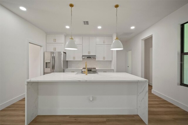 kitchen featuring hardwood / wood-style floors, an island with sink, stainless steel appliances, white cabinetry, and light stone counters