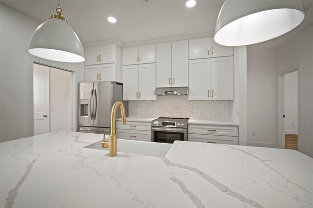 kitchen featuring decorative light fixtures, light stone countertops, backsplash, appliances with stainless steel finishes, and white cabinetry